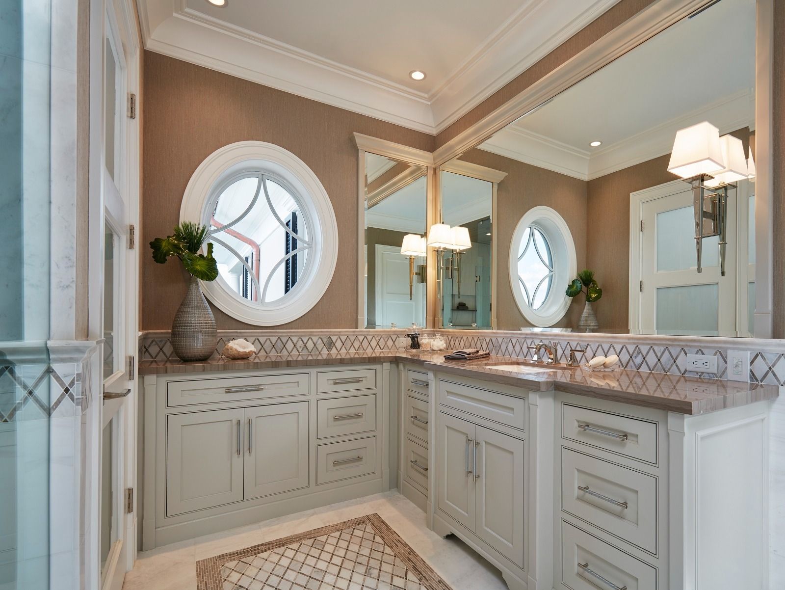Bathroom with two oval windows, large mirror, light-colored cabinets, and brown walls.
