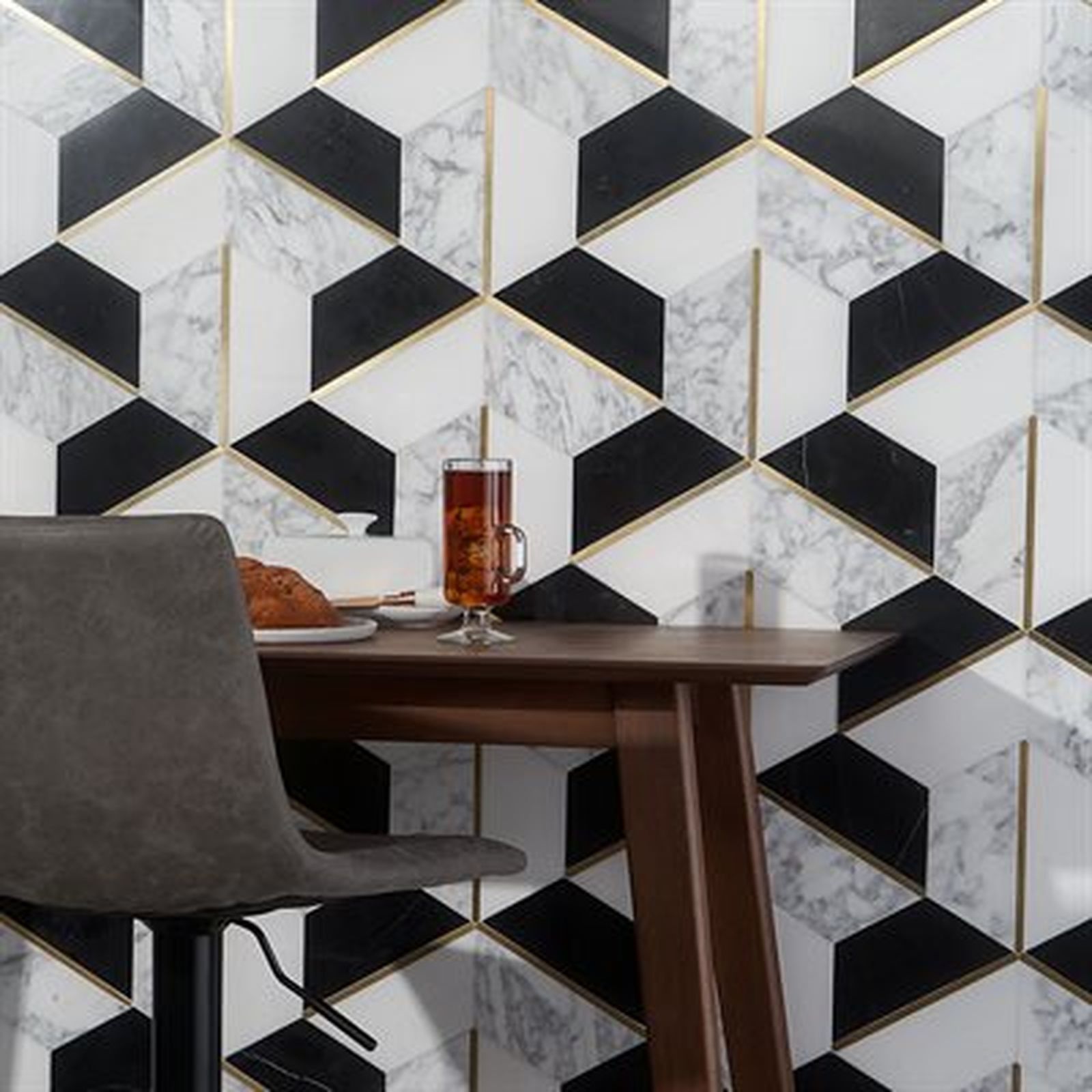 Black and white geometric wall tile with gold accents, beside a wooden table with a chair, and a drink.