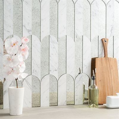White marble and mirrored tile backsplash with orchids, cutting board, and olive oil.