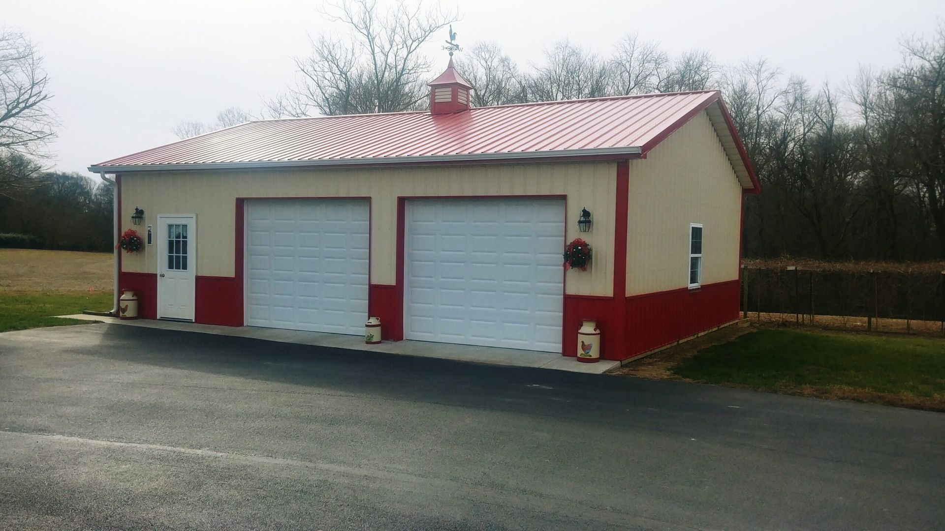 Small red-and-cream garage building with two white doors beside a paved driveway and trees