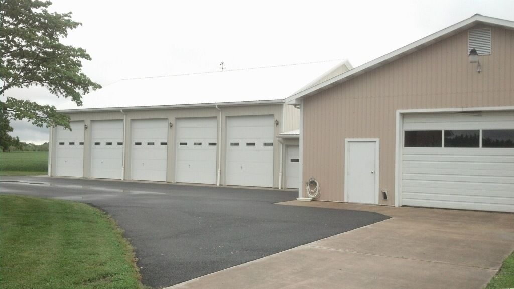 White garage building with multiple bay doors and a driveway on a cloudy day