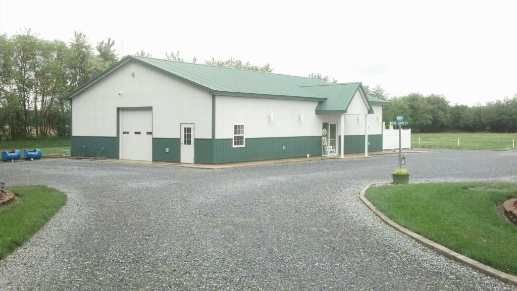 Gravel driveway leading to a white and green building with garage doors in a rural setting.