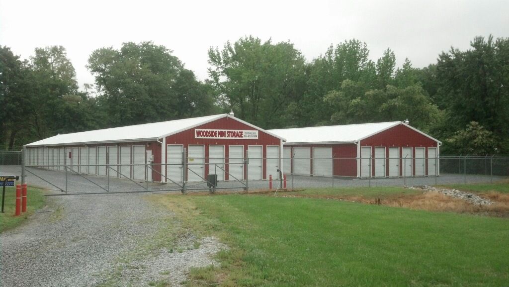Red-and-white barn-style building on a grassy field near a gravel path and trees under cloudy skies