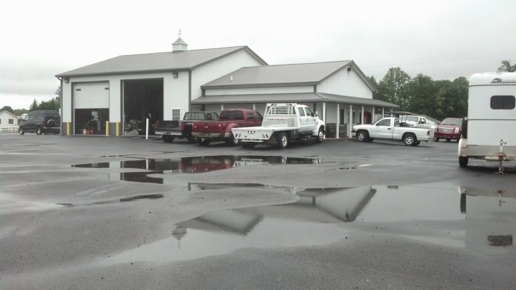 Gray parking lot with puddles in front of a white building and parked cars on an overcast day
