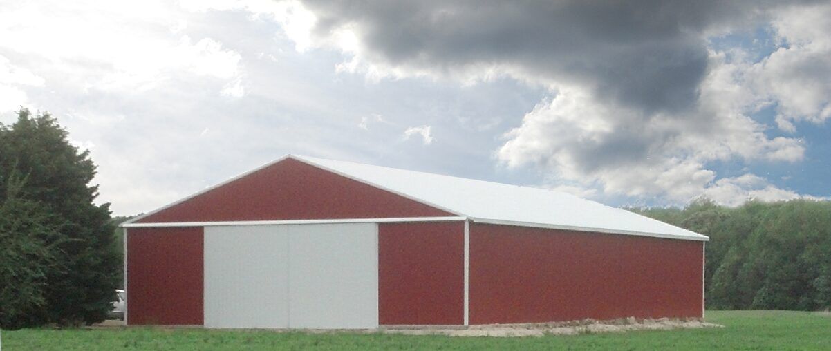 Red barn with white roof and doors on a grassy field under a cloudy sky