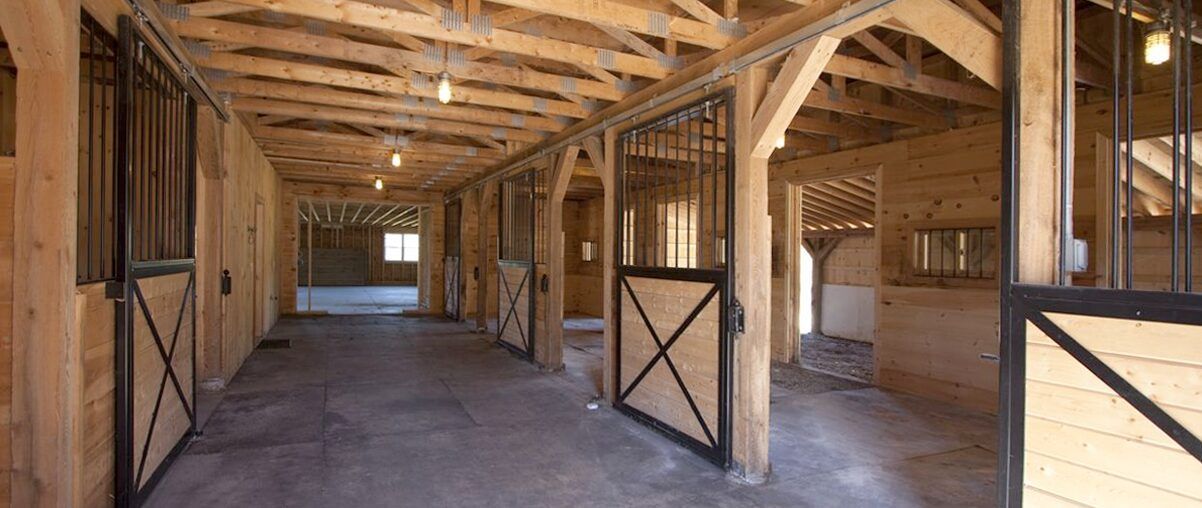 Empty wooden barn interior with stalls, exposed beams, and a concrete floor