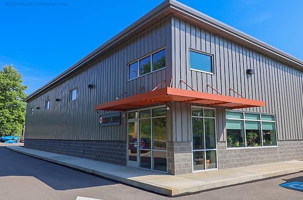 Modern gray industrial building with orange awning and large windows on a sunny street corner
