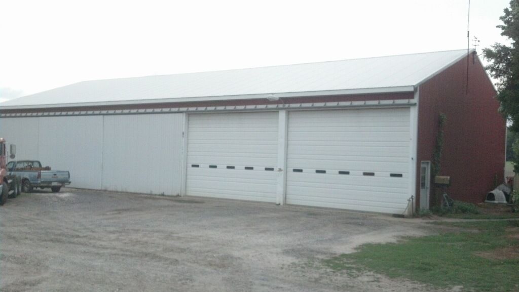 Large white metal barn with red end wall on a gravel lot, viewed from the side.