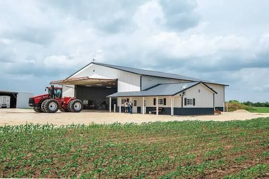 Red tractor parked by a white barn in a rural field under cloudy skies