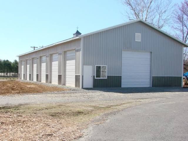 Gray metal warehouse with multiple roll-up doors and a large garage door on a gravel lot
