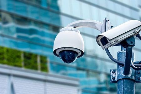 Dos cámaras de seguridad están montadas en un poste frente a un edificio.