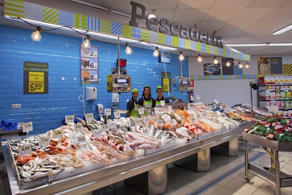 Un grupo de personas está de pie frente al mostrador de pescado de una tienda.