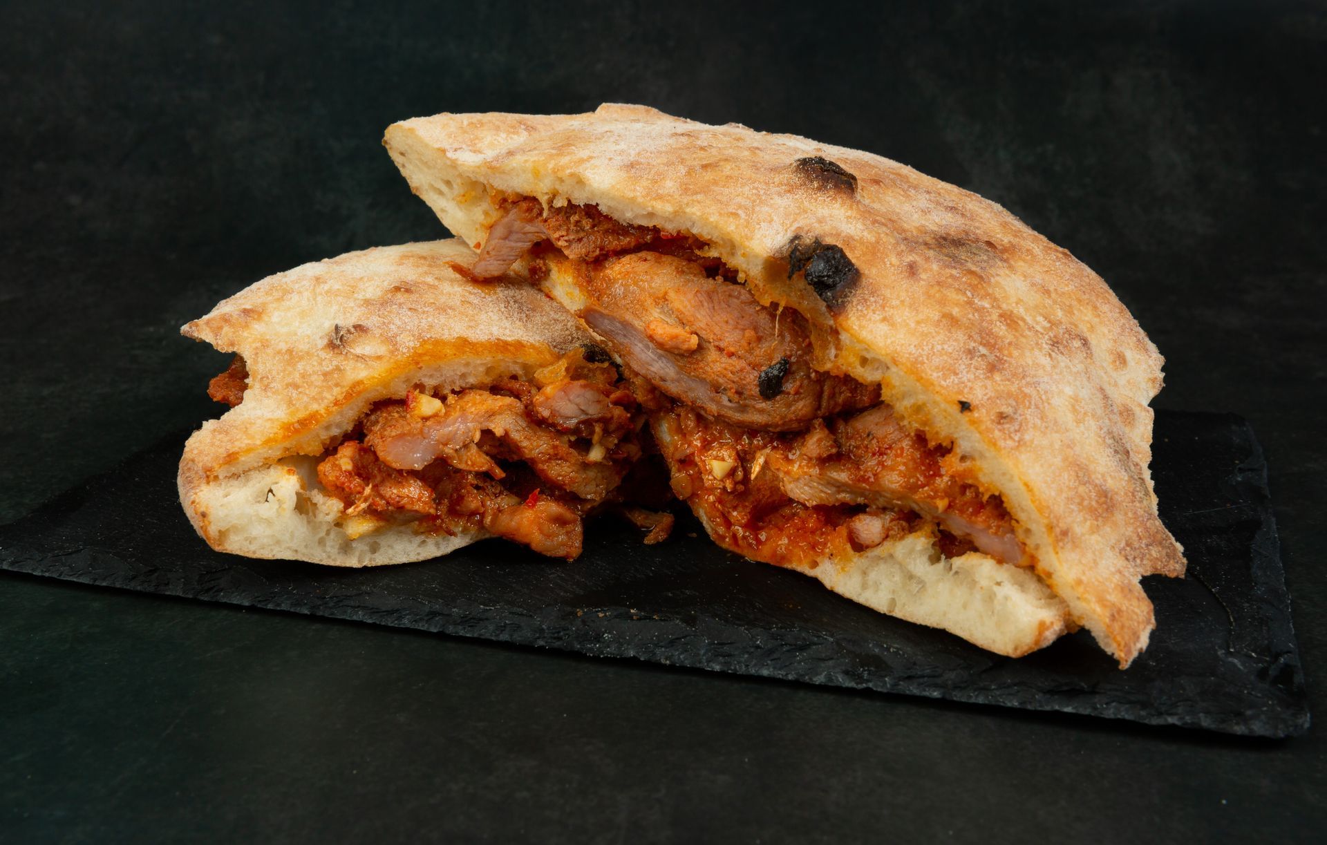 Deux moitiés de pita farcies à la viande et à la sauce, posées sur une ardoise noire.