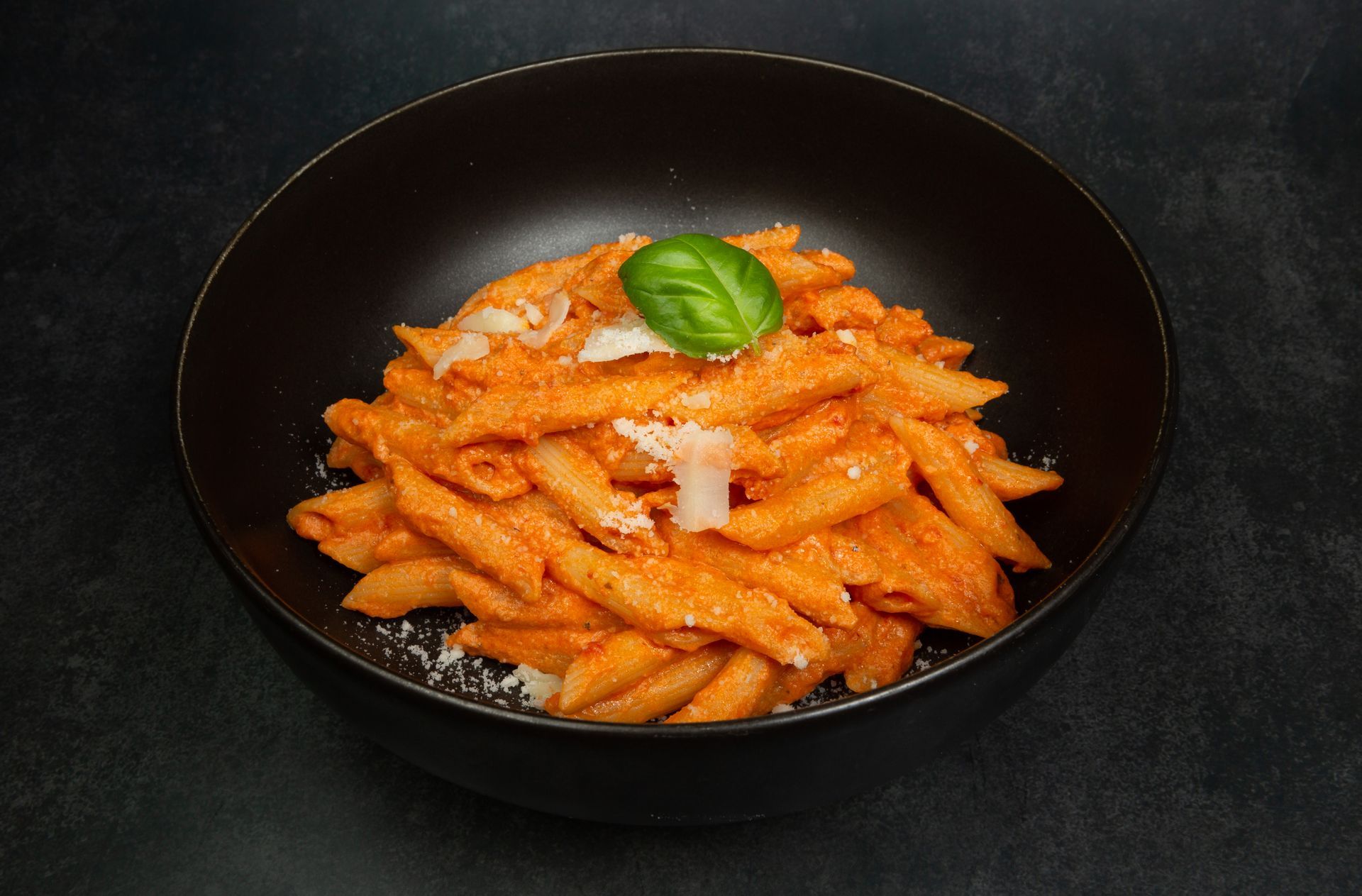 Pâtes penne à la sauce tomate et au basilic dans un bol noir sur fond sombre