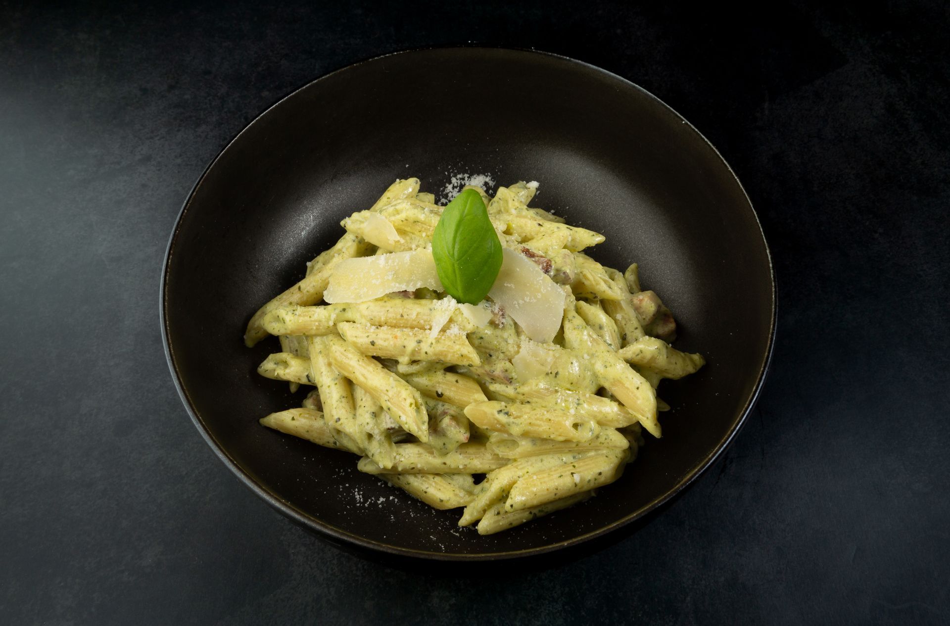 Pâtes penne à la sauce crémeuse garnies de basilic, servies dans un bol noir