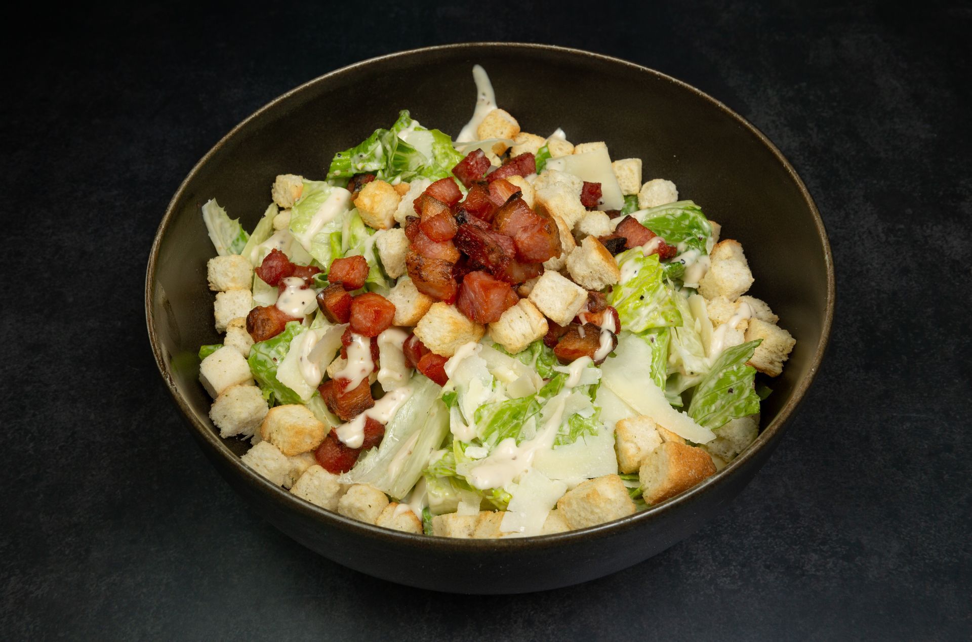 Salade composée de laitue, de croûtons, de pommes de terre en dés et de bacon sur fond sombre