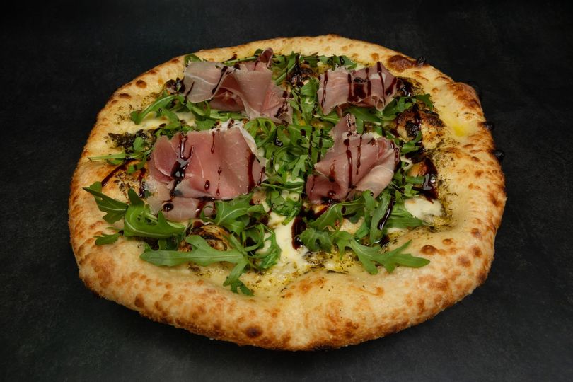 Pizza garnie de prosciutto, de roquette et d'herbes sur fond sombre