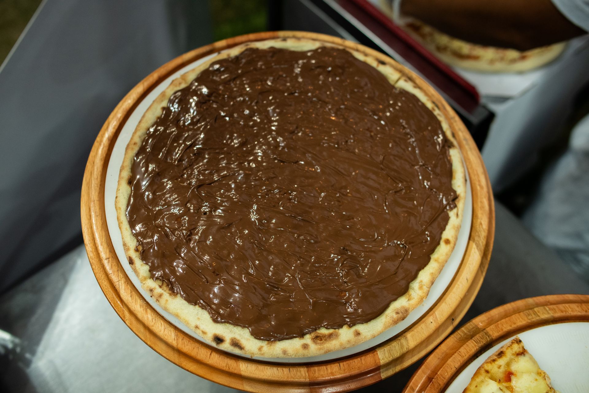 Dessert rond nappé de pâte à tartiner au chocolat, présenté sur une assiette en bois, avec une petite cuillère sur le bord.