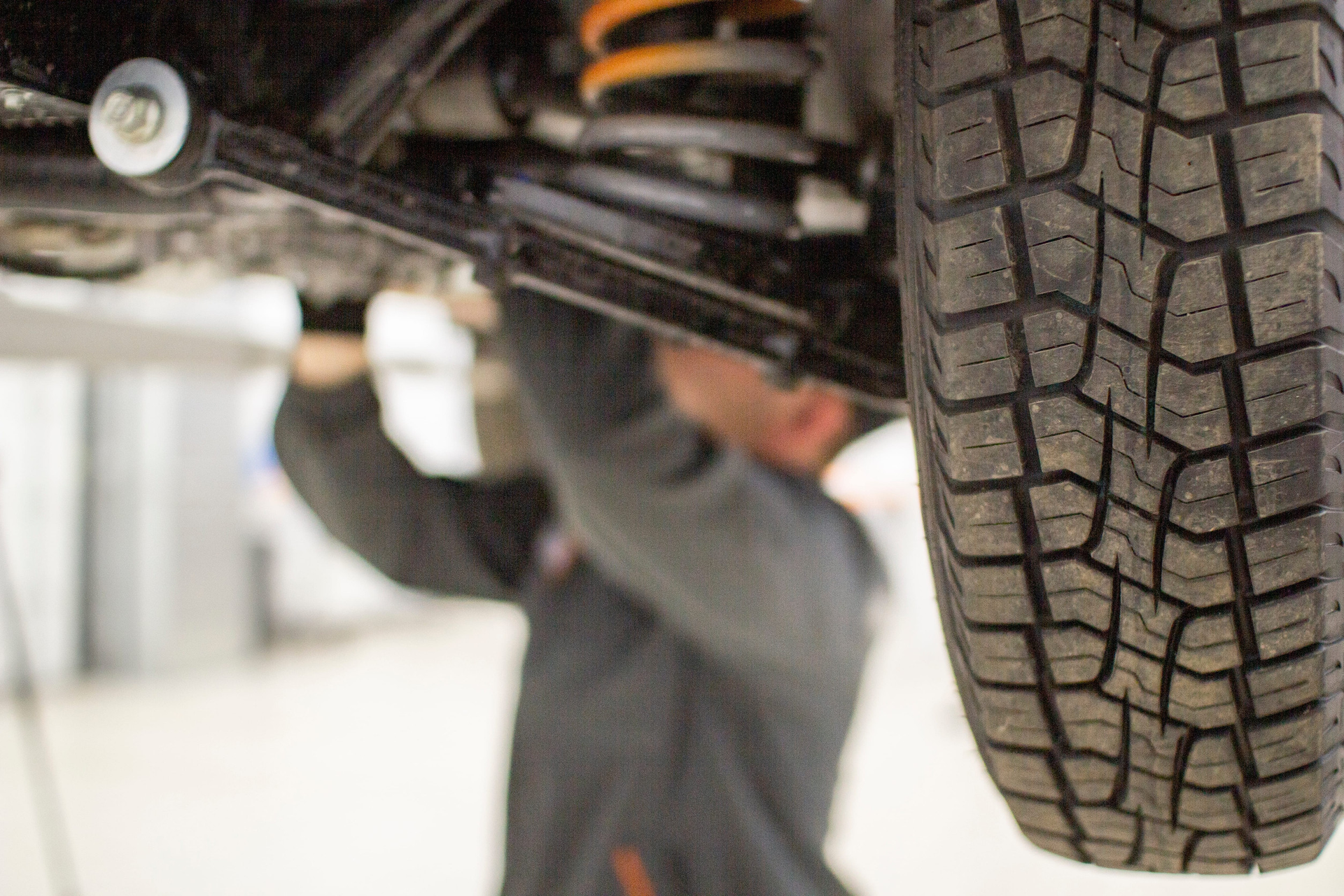 A mechanic works on the suspension system and tire of a vehicle raised on a lift in a workshop.