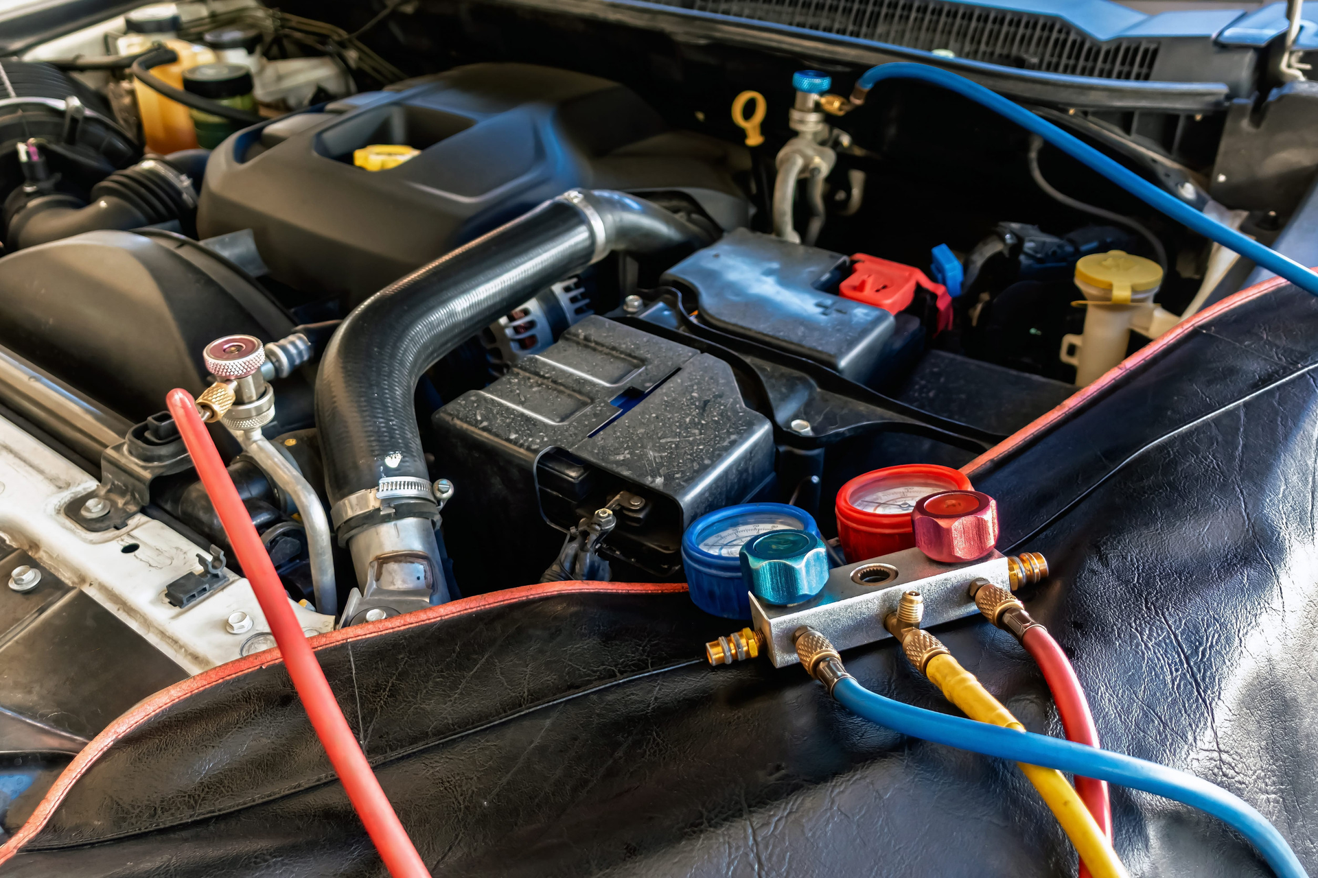 An automotive air conditioning manifold gauge set connected to an engine bay for maintenance and testing.