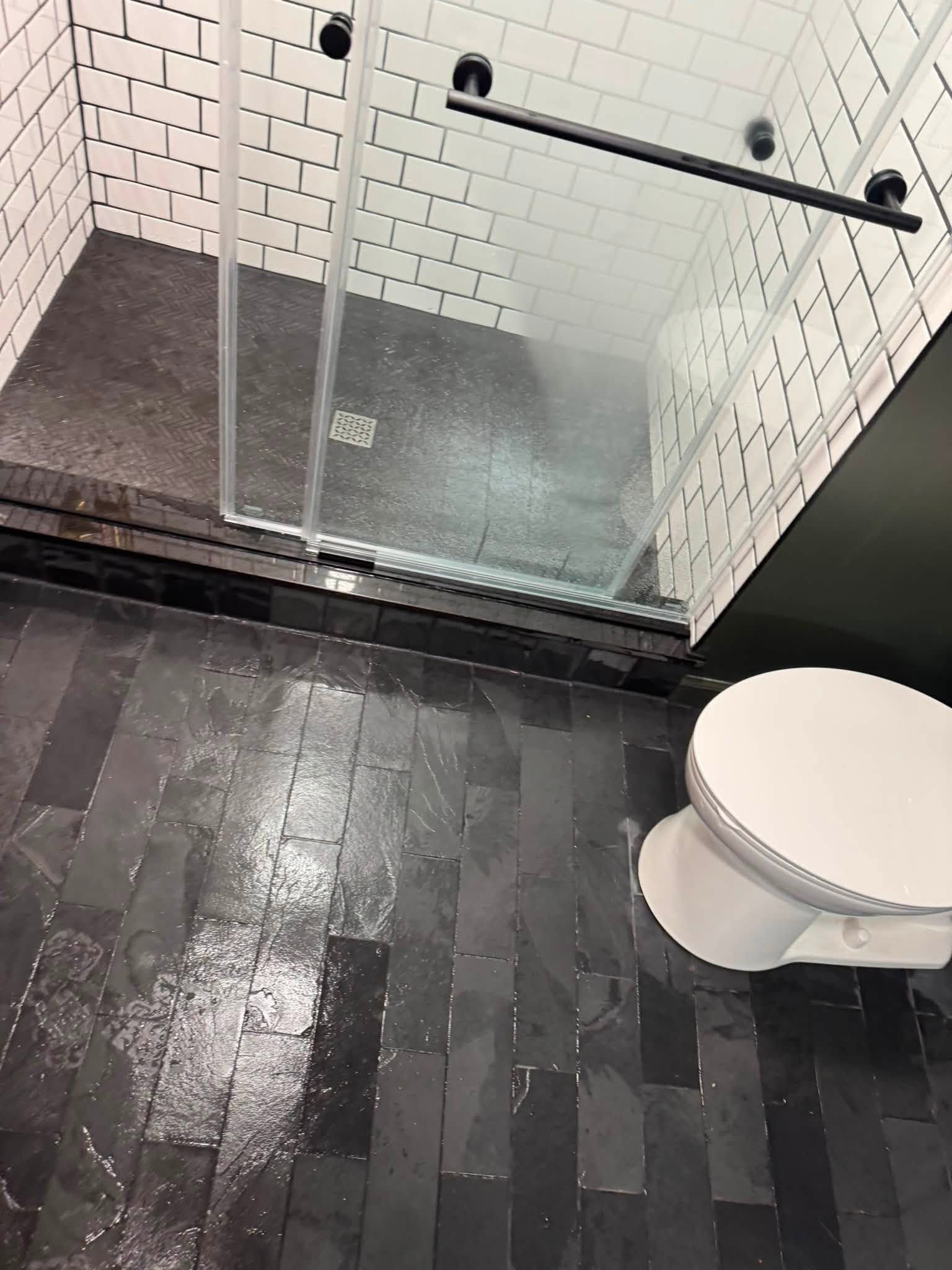 Small bathroom with glass shower, dark tile floor, white brick walls, and a toilet.