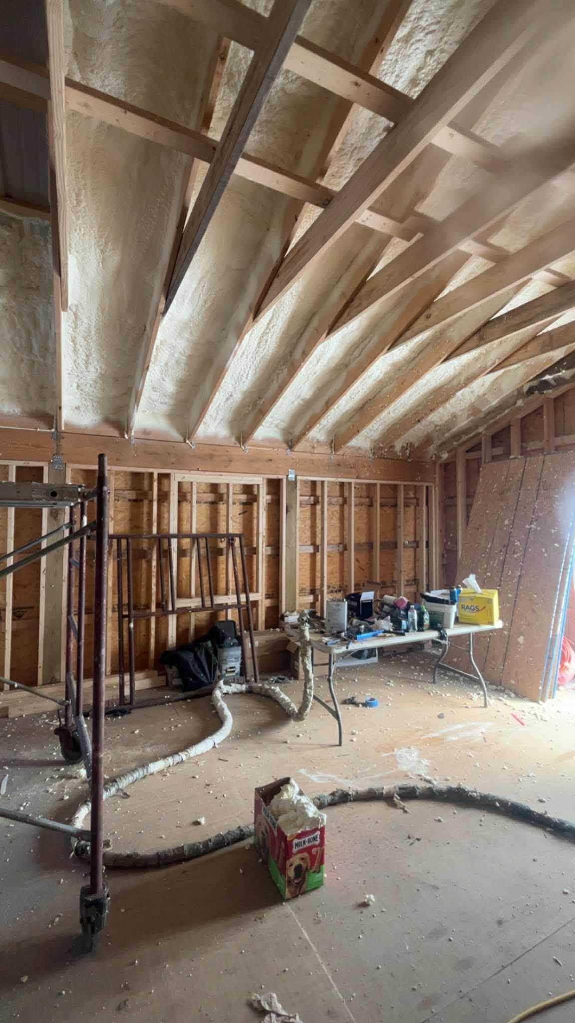 Partially finished room under construction with exposed framing, rafters, tools, and debris on the floor