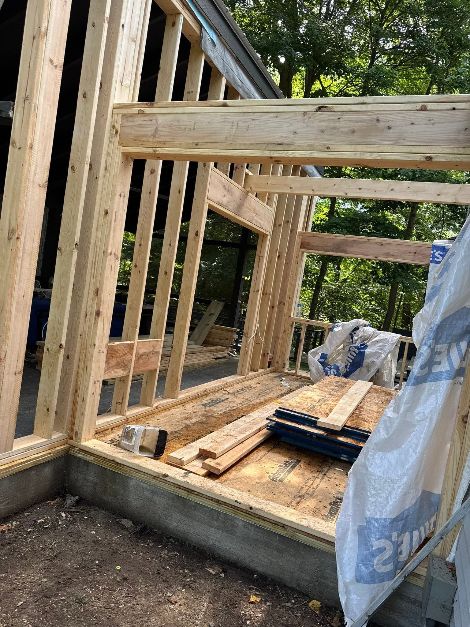 Wood-framed house under construction with concrete foundation and a tarp draped over materials
