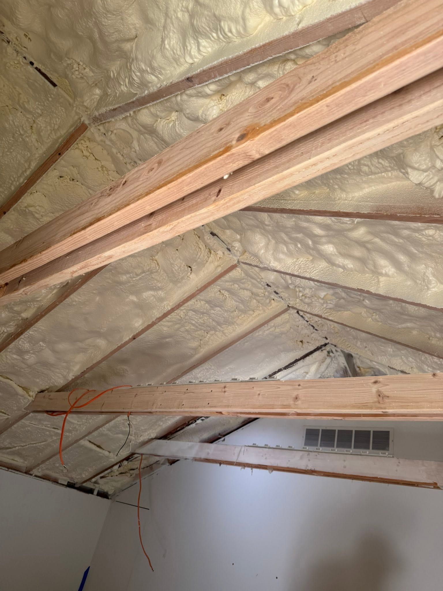 Exposed attic ceiling with wooden rafters, insulation, and a vent above a white wall