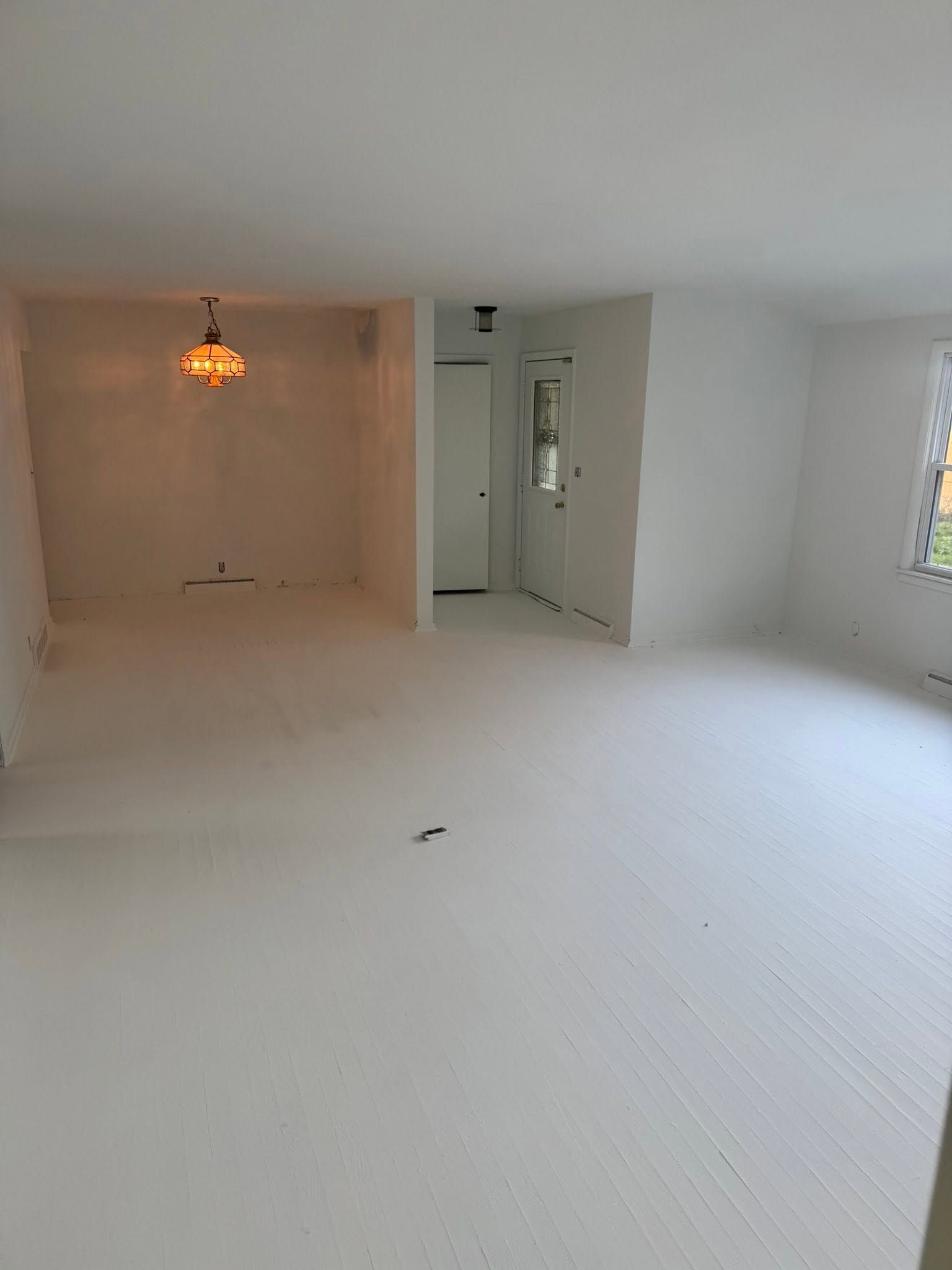 Empty white room with textured floor, recessed alcove, and a small hanging light fixture.