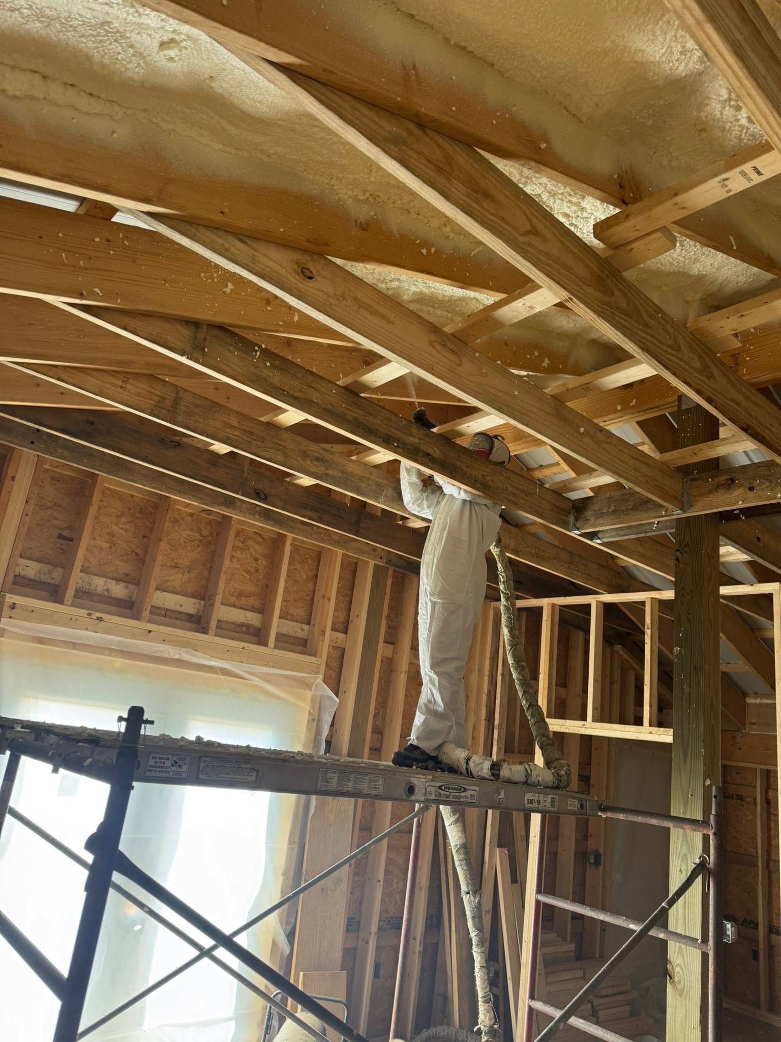 Interior of a house under construction with exposed wooden framing and insulation in the ceiling.
