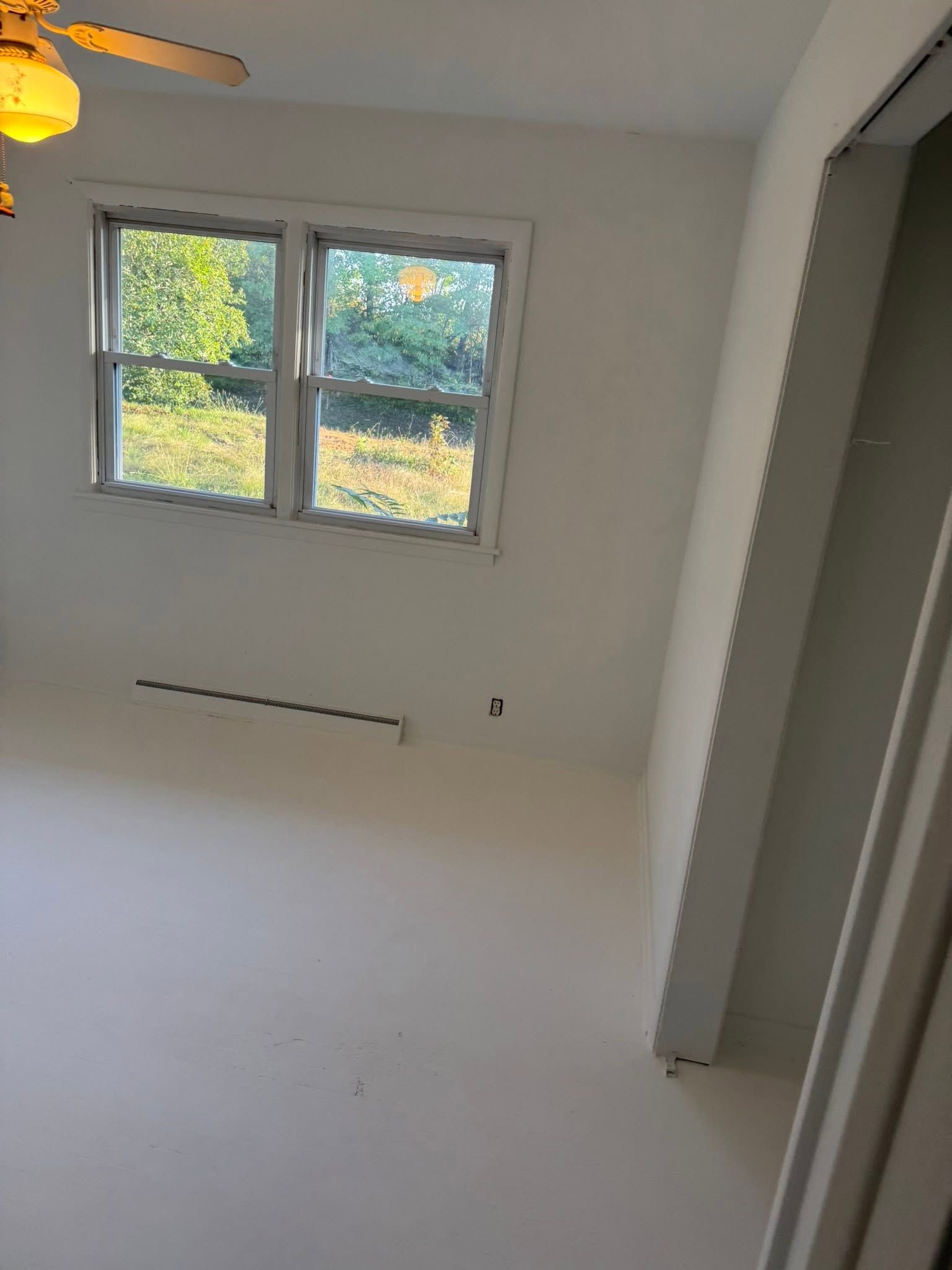 Empty white room with a window, ceiling fan, and bright natural light.