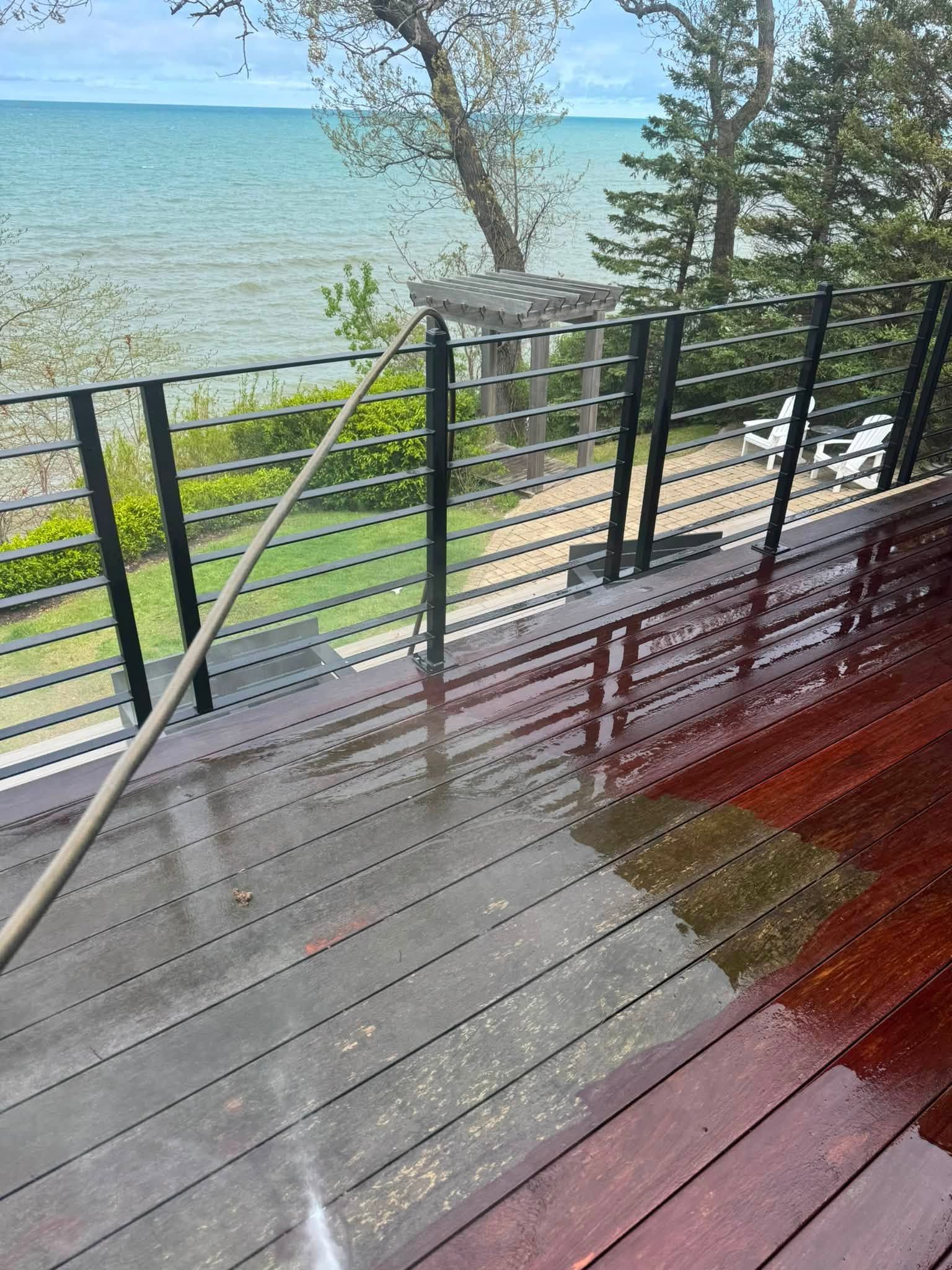 Wet wooden deck with black railing overlooking a lake and trees