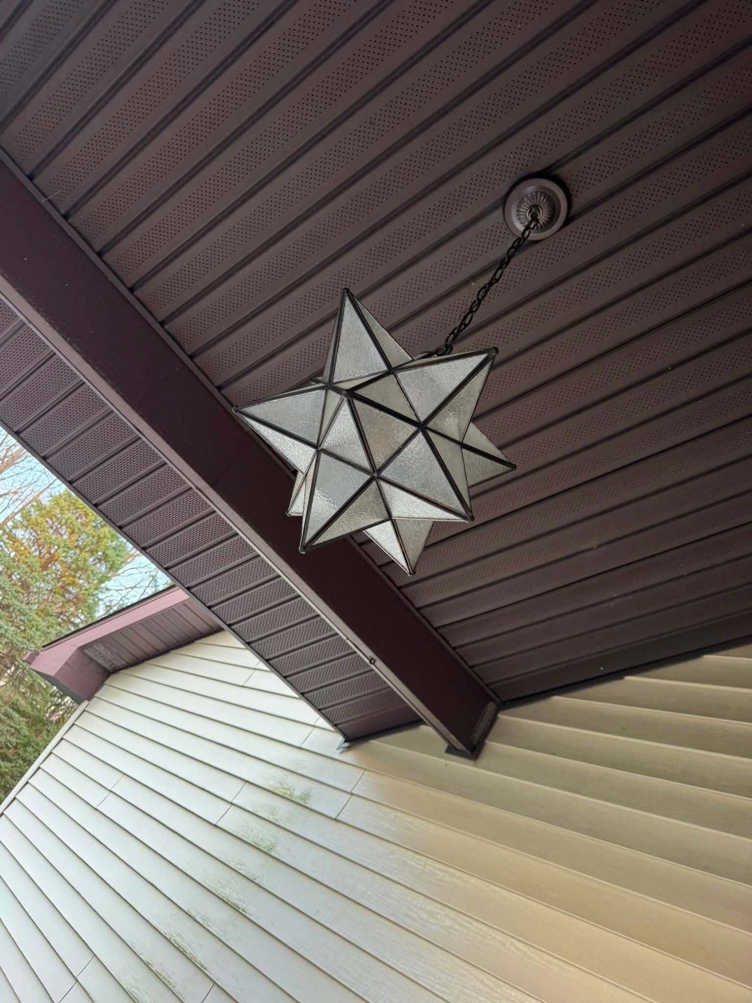 Hanging white star ornament under a brown porch roof beside beige siding.