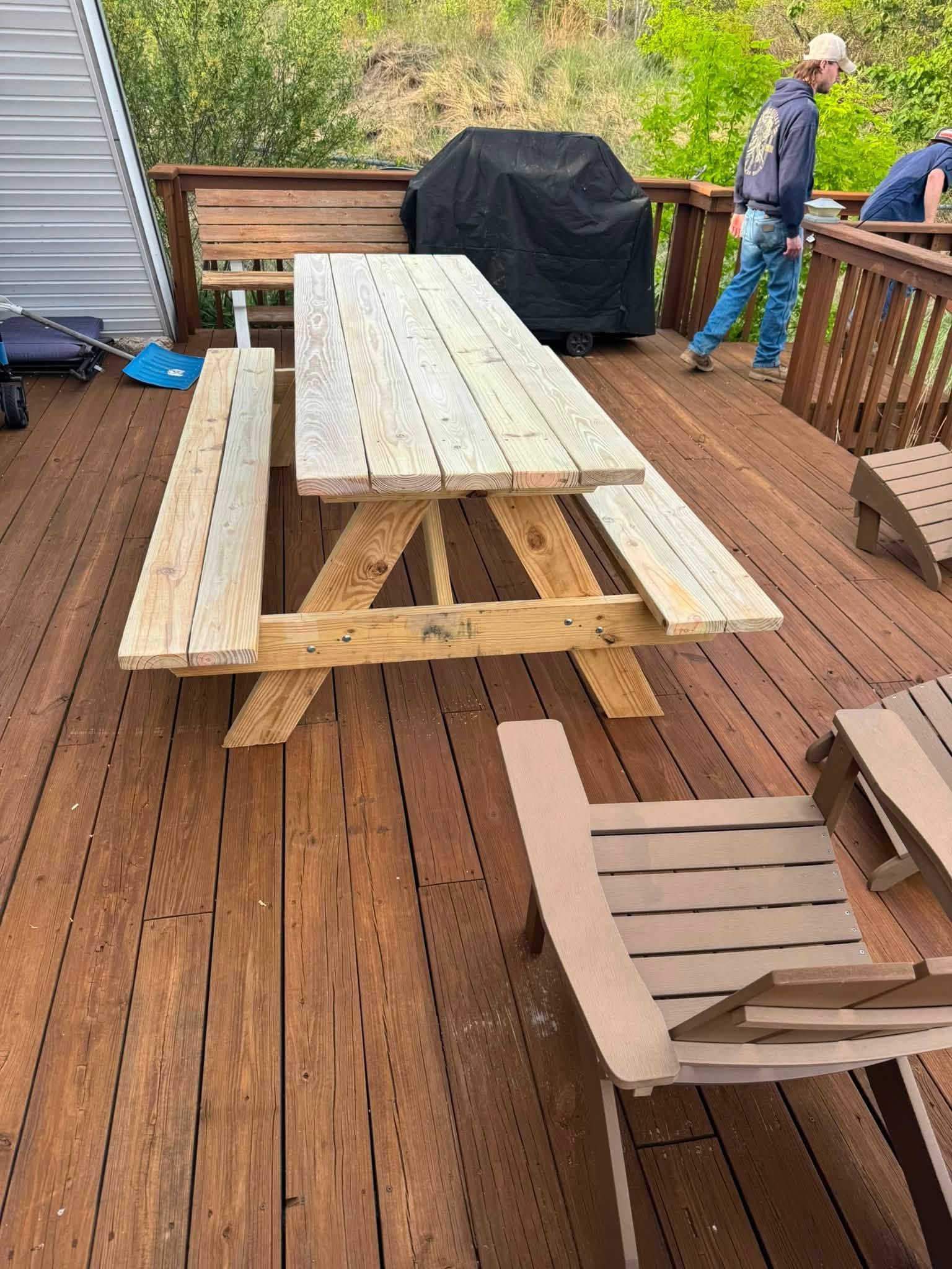 Wooden deck with a picnic table, covered grill, and a person standing near the railing