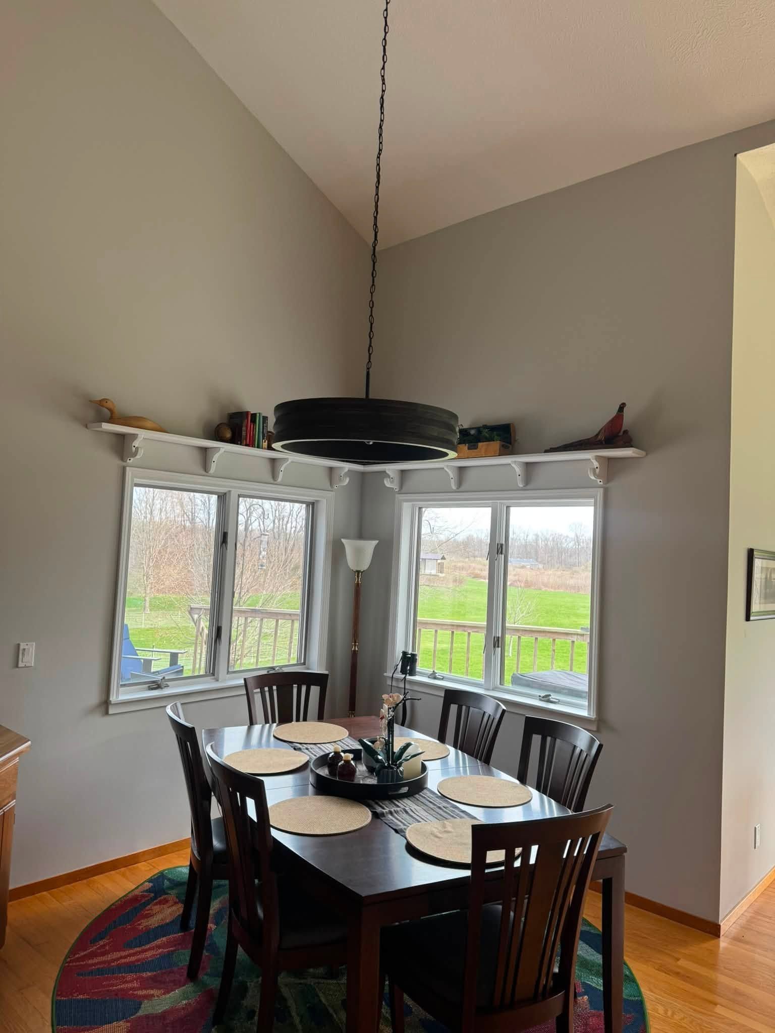 Dining room with round table, chairs, and large corner windows overlooking a field