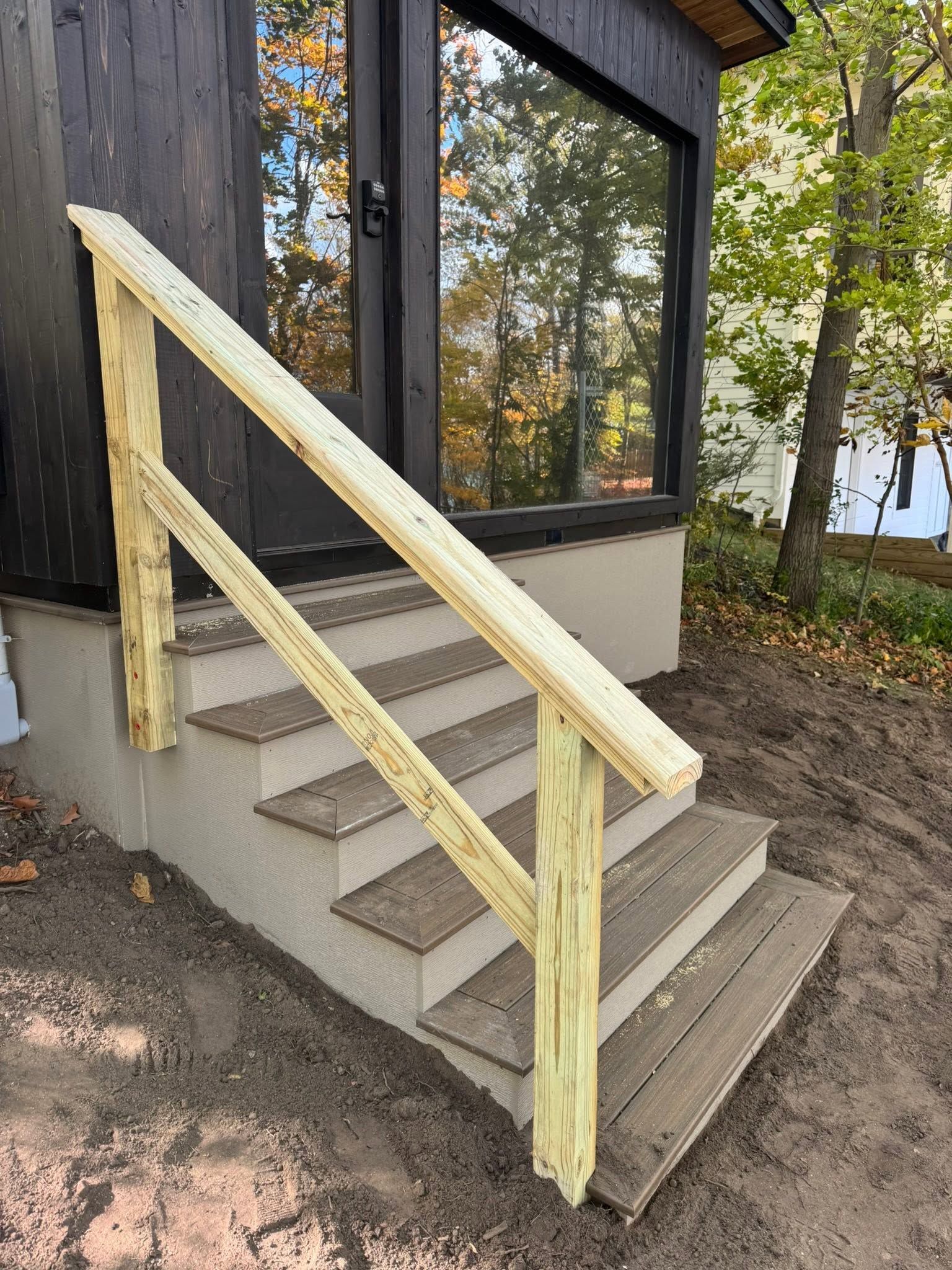 Yellow wooden handrails on concrete steps leading to a building entrance by trees and water.