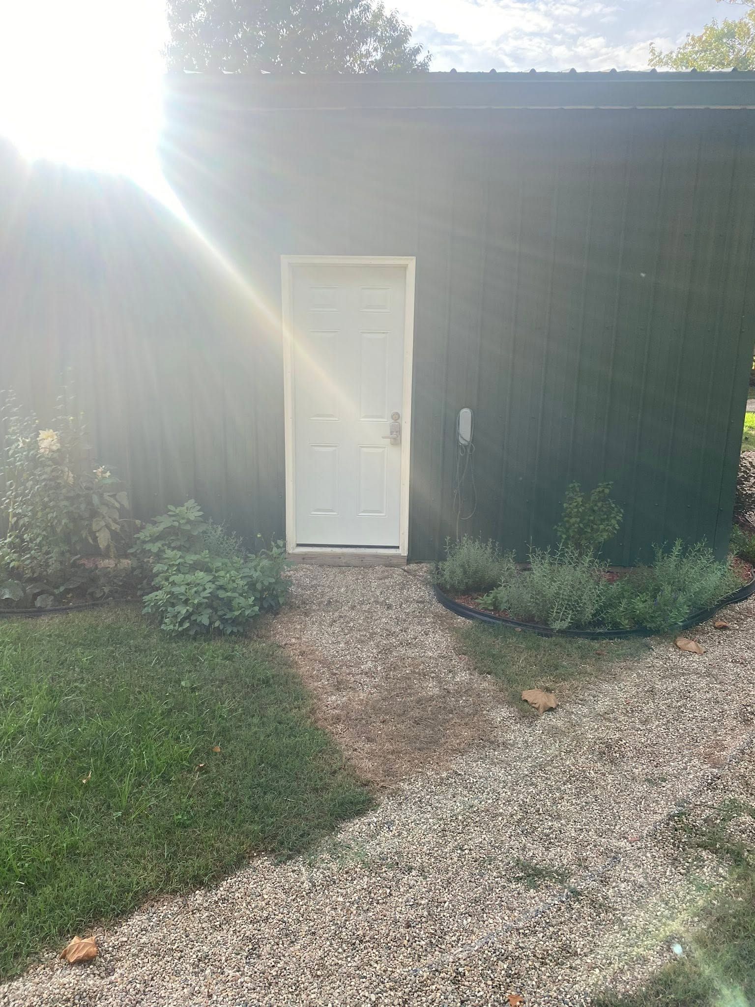 White door on a dark building with a gravel path and bright sunlight glare.