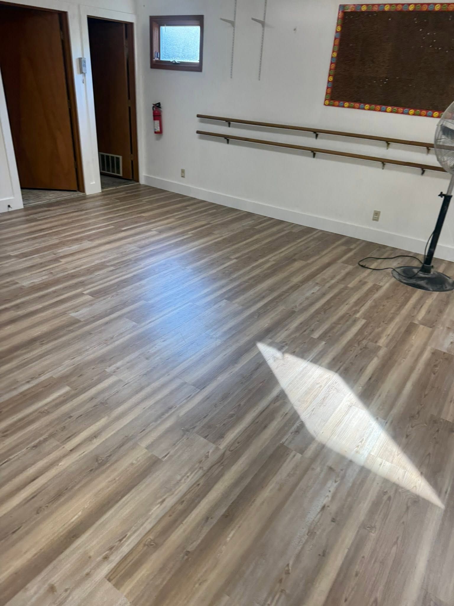 Empty dance studio with wood floors, mirrors, ballet barres, and bright sunlight on the floor