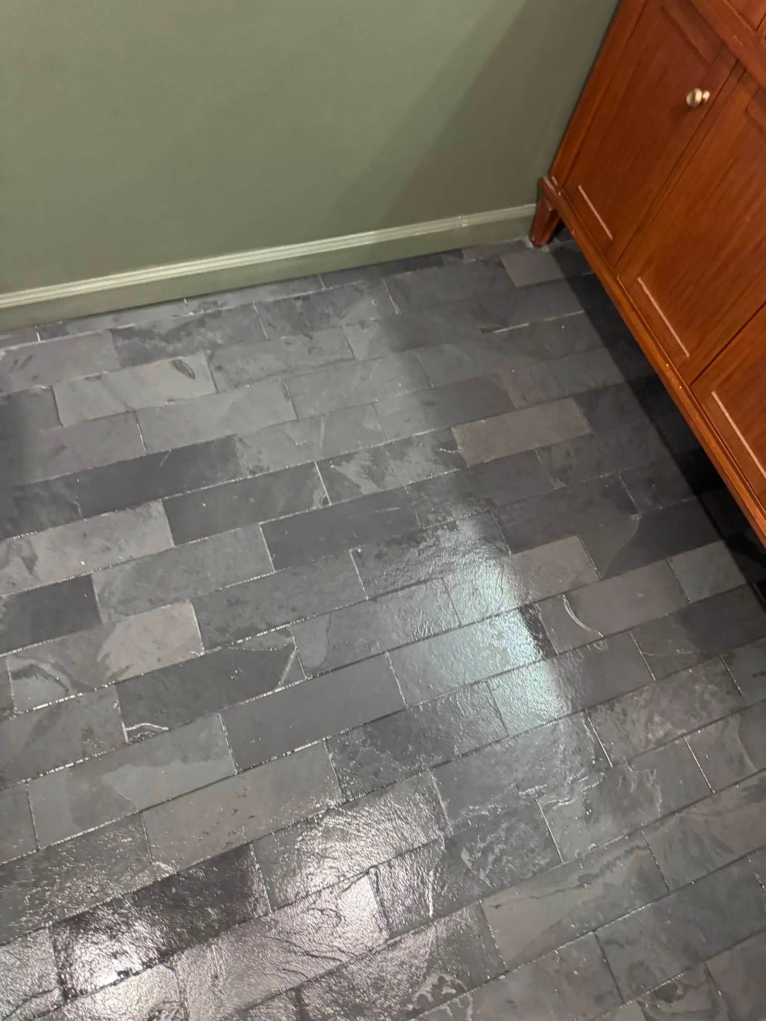 Wet gray tile floor beside a wooden cabinet and baseboard heating unit