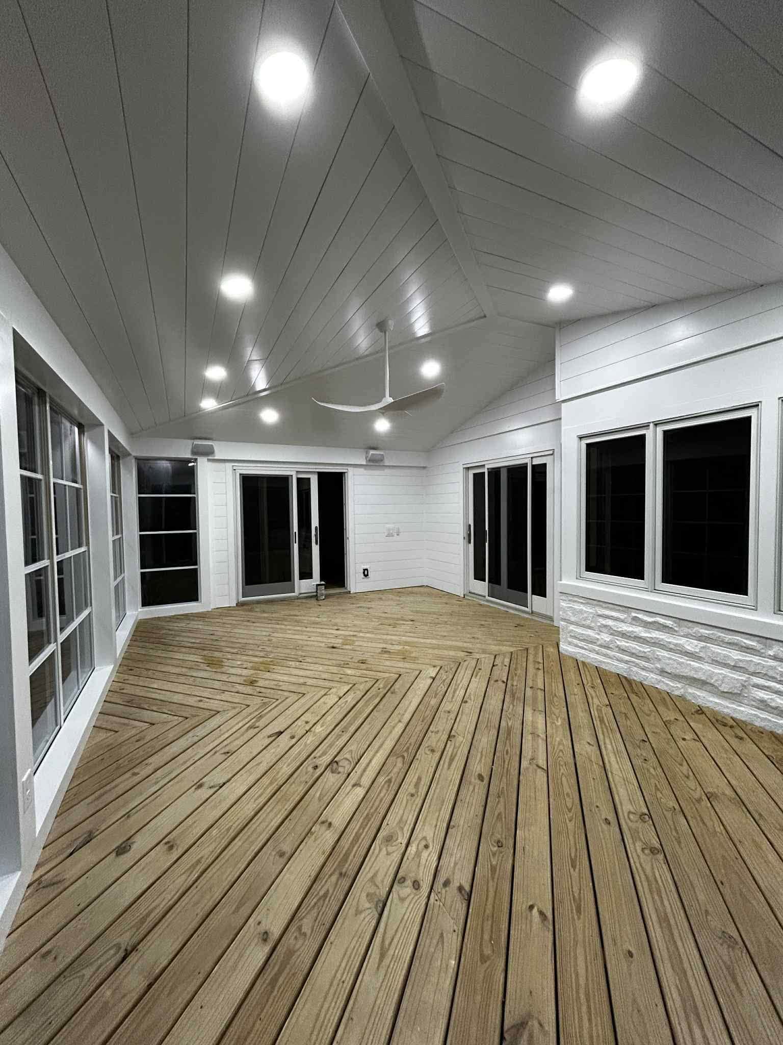 Empty enclosed sunroom with white walls, recessed lights, and unfinished wood floor under construction