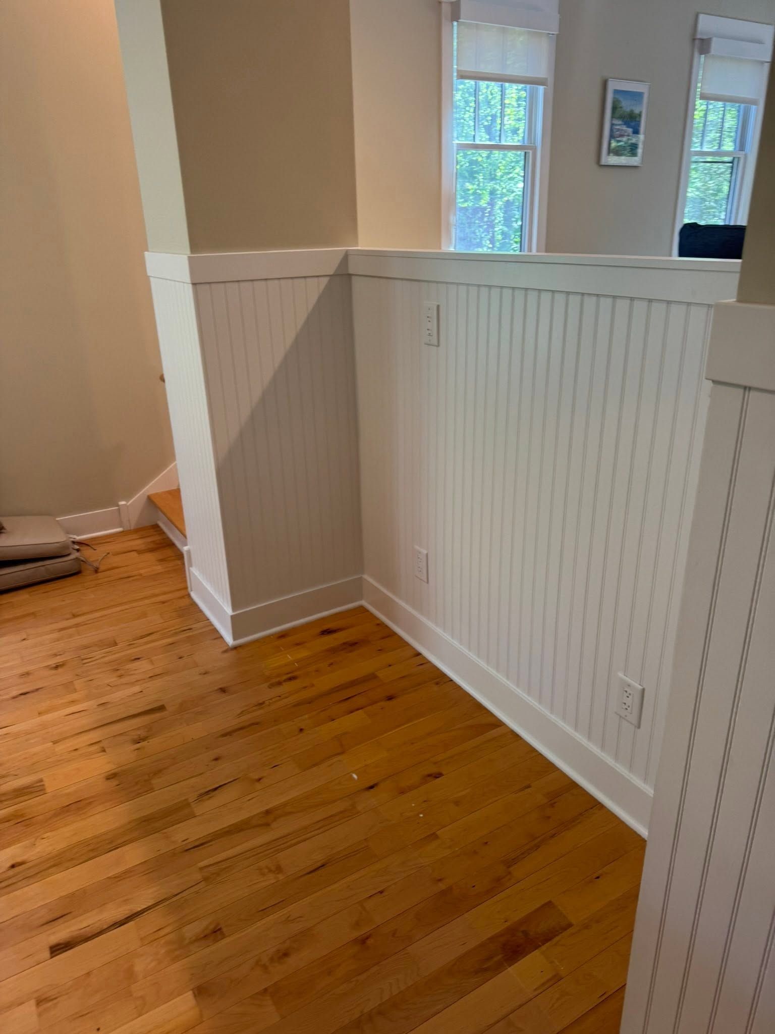 Interior hallway with hardwood floor and white wainscoting, open view to adjacent rooms.