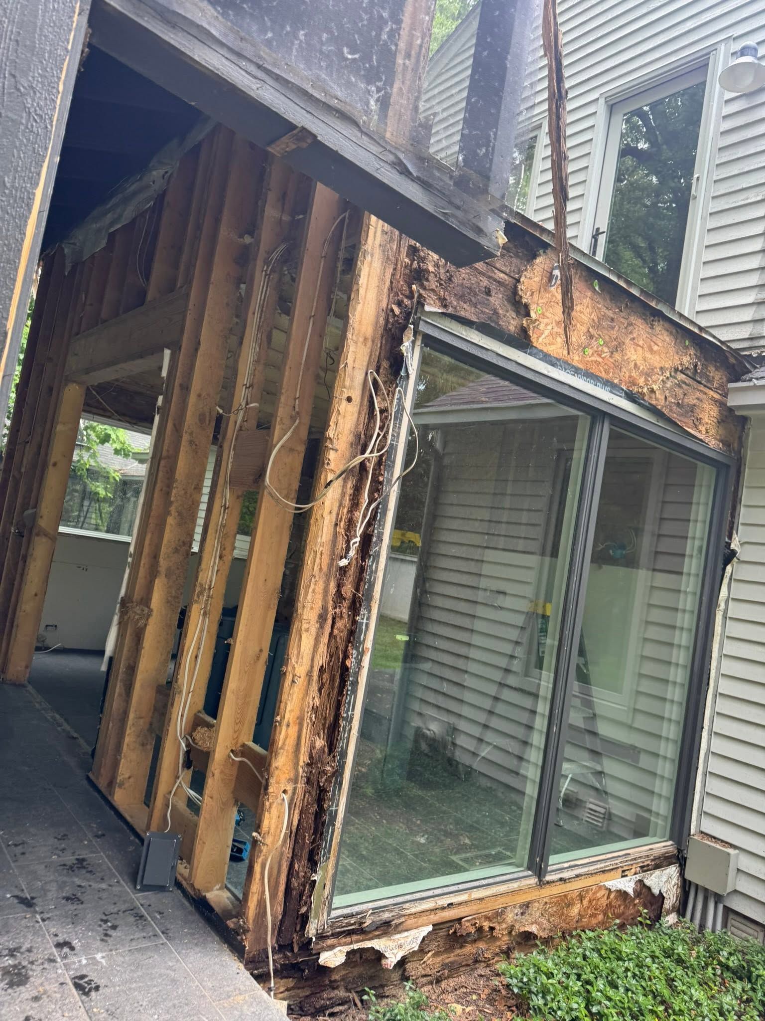 Damaged exterior wall with exposed wood framing and a large sliding glass door on a slanted building edge