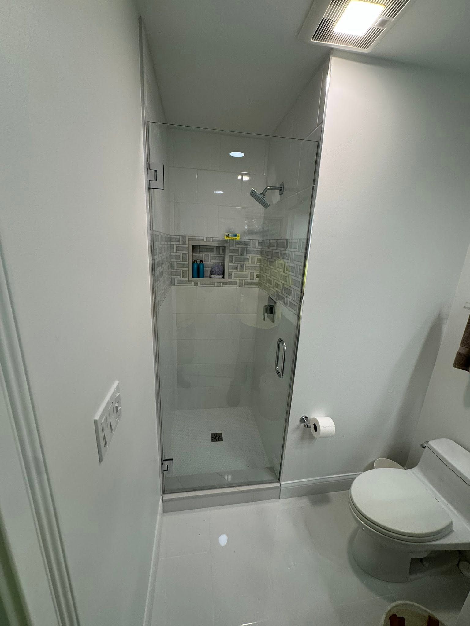 Small modern bathroom with glass shower, white tile, and toilet beside the shower door.