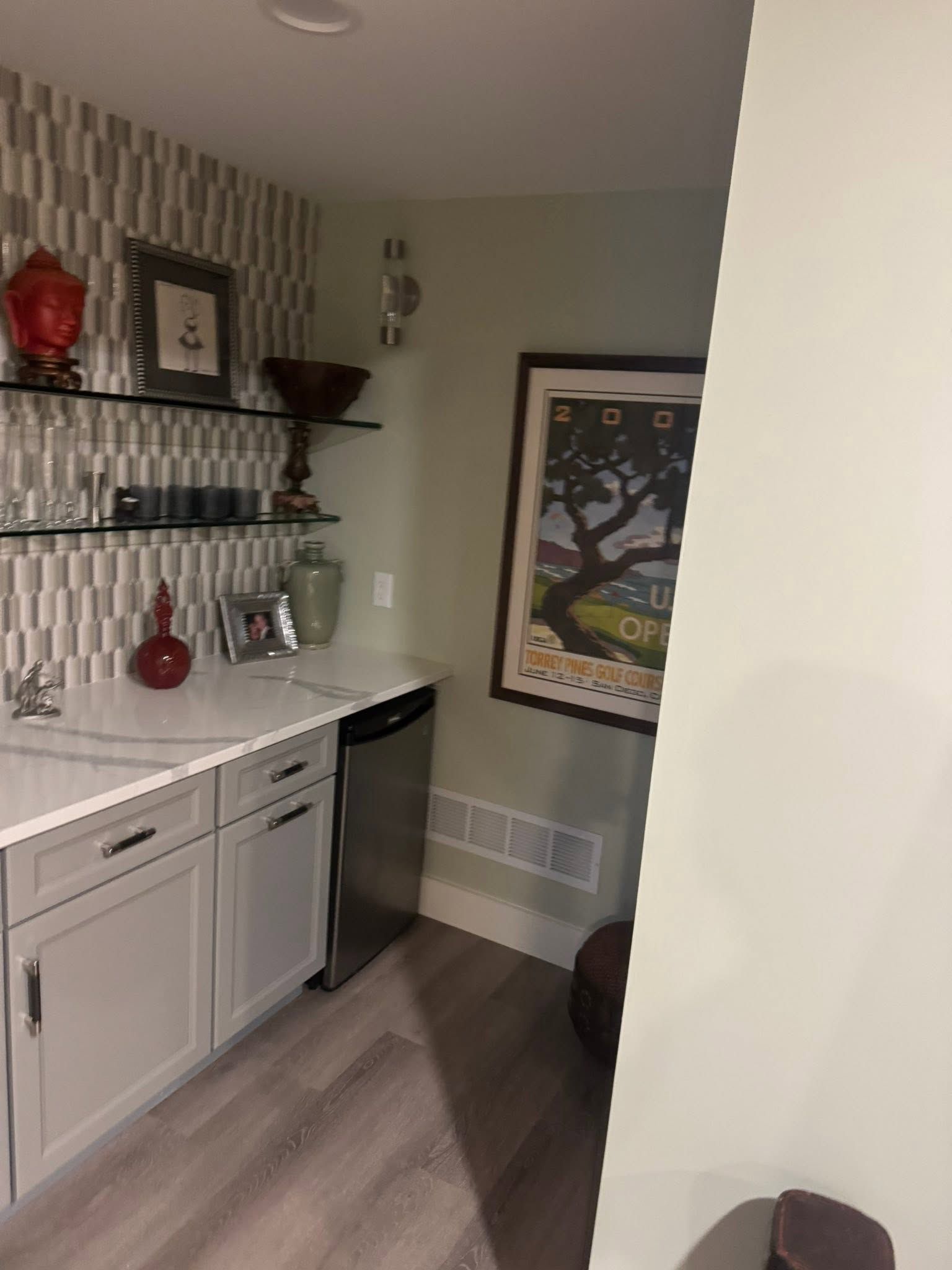 Small home bar nook with white cabinets, shelves, a mini fridge, and framed wall art.