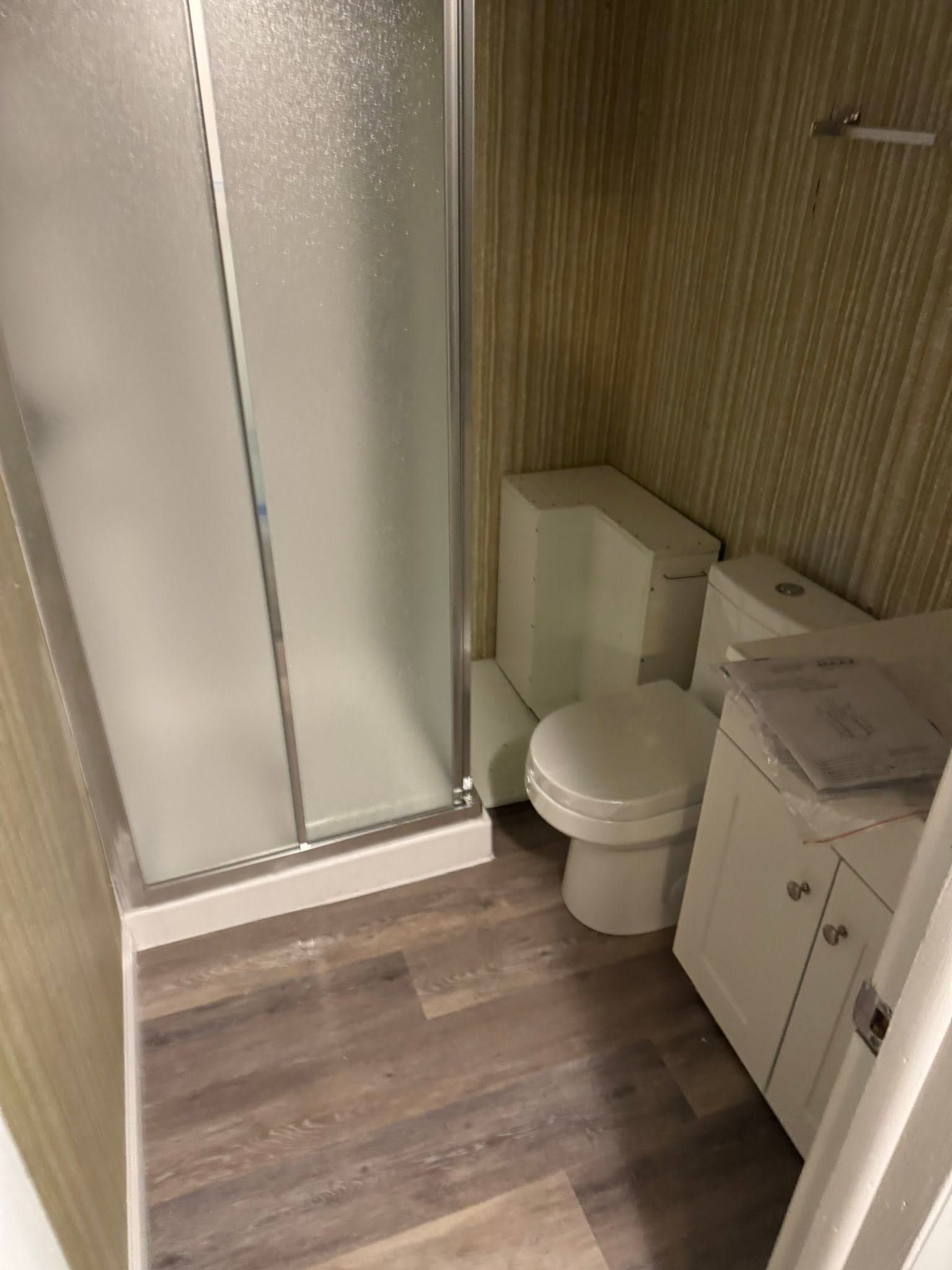 Small bathroom with frosted shower doors, toilet, and white vanity beside wood-paneled wall.
