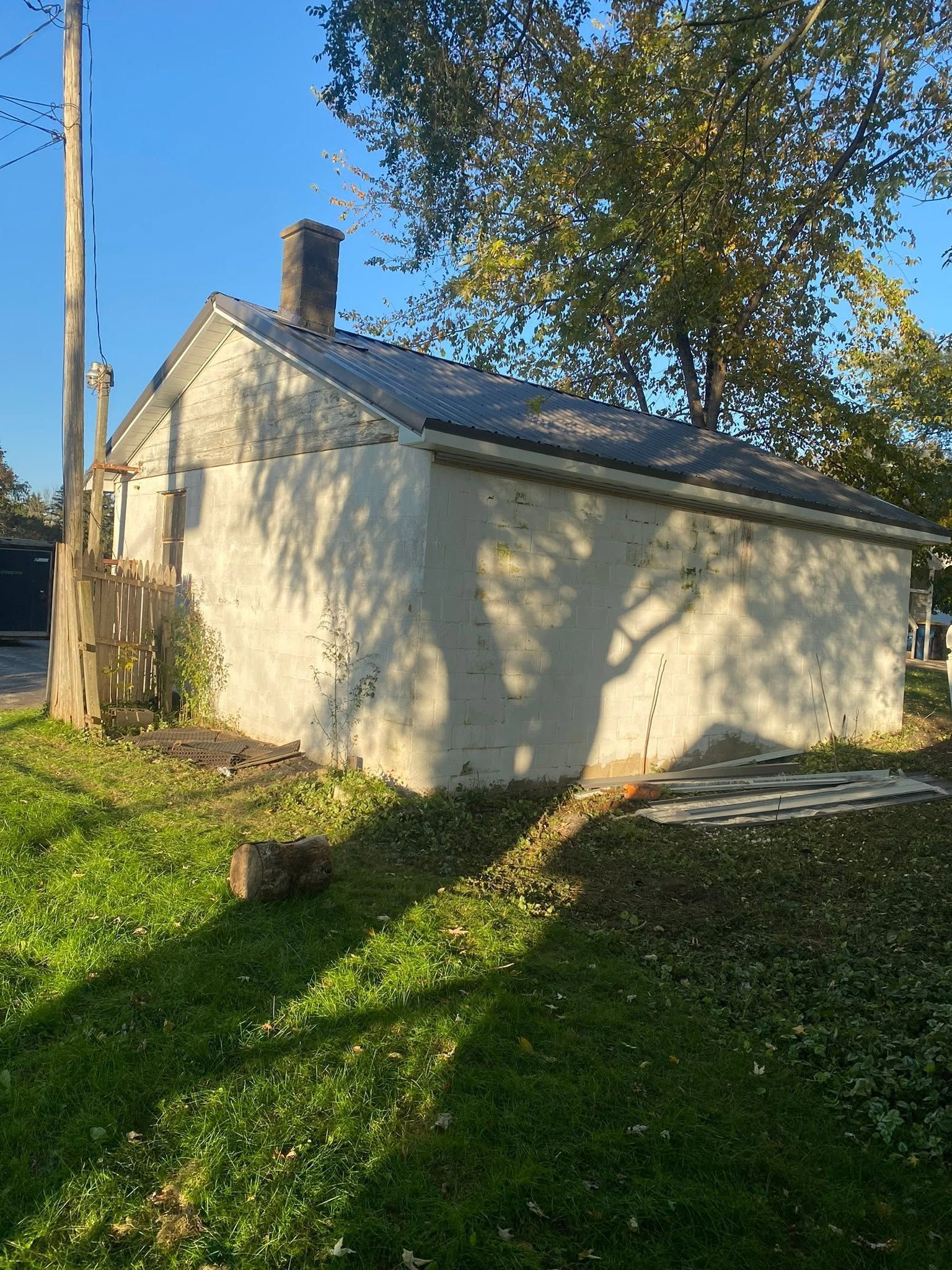 Small beige house with a sloped roof and chimney, lit by sun in a grassy yard with trees.
