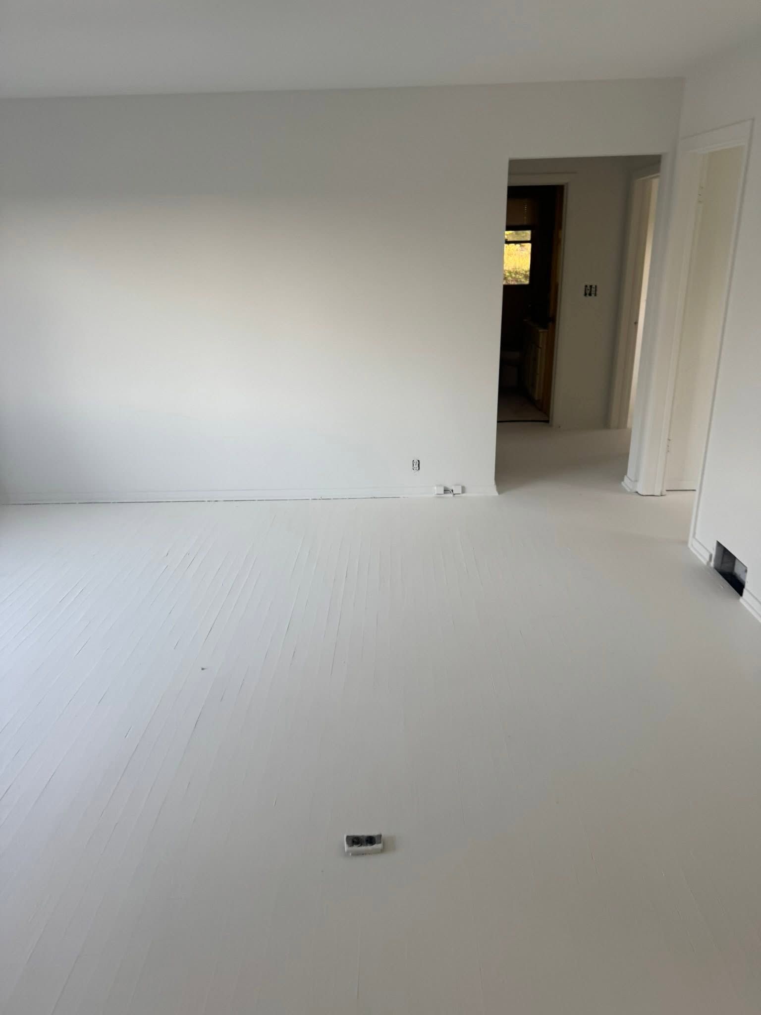 Empty white room with unfinished floor, open doorway, and built-in closet door on the right.