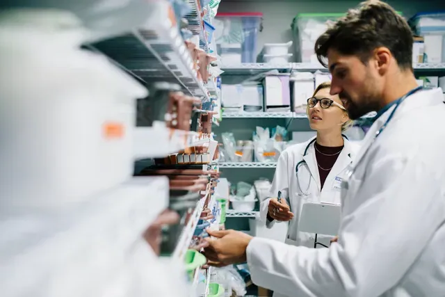 Scientists in white lab coats working in a laboratory aisle among shelves of supplies.