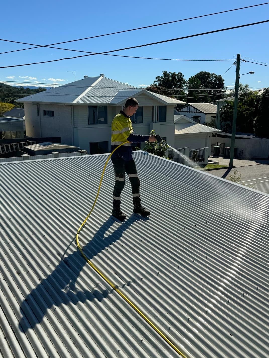 A man is spraying water on a roof with a hose.
