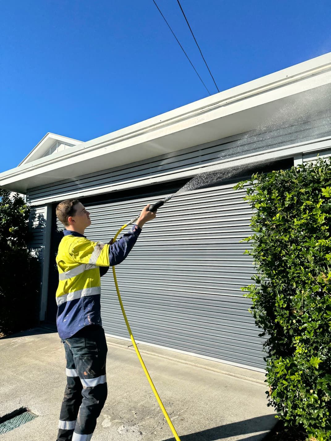A man is spraying water on a garage door with a hose.
